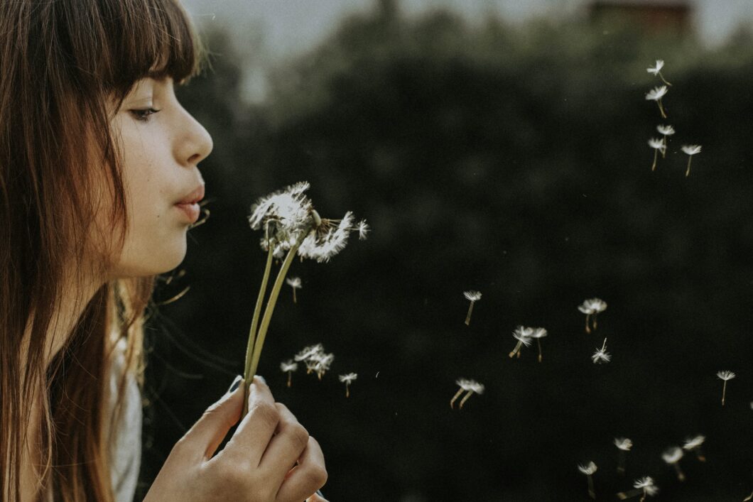 une femme respire et souffle sur une fleur pour disperser ses graines